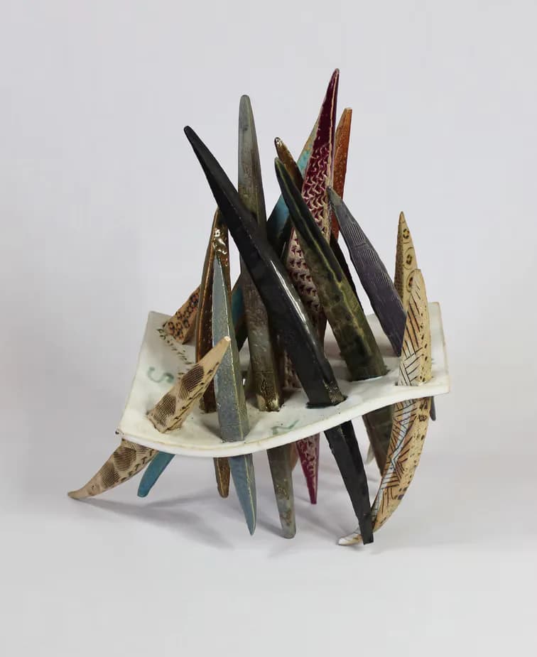 Ceramic sculpture with spiked colored elements rising from a curved white base