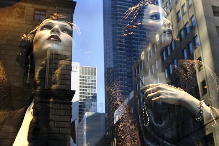 Two mannequin heads with reflective surfaces positioned in an urban street, photographed by Adam Reyes; skyscrapers visible in background through glass reflections.