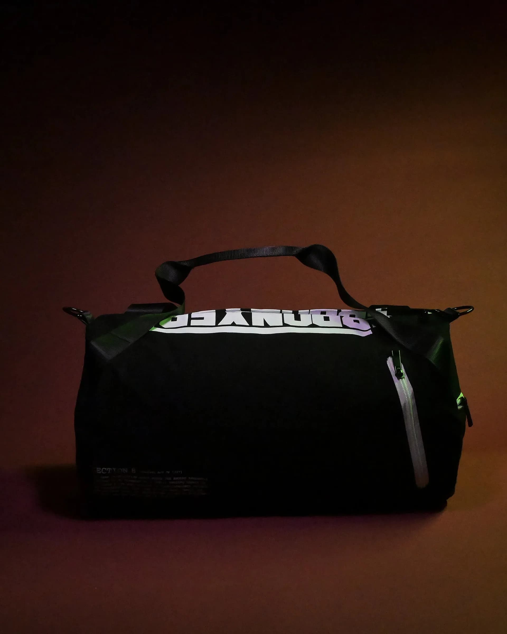 Black duffel bag with white ribbed texture and 'CHANUKK' text visible, photographed against warm brown backdrop.