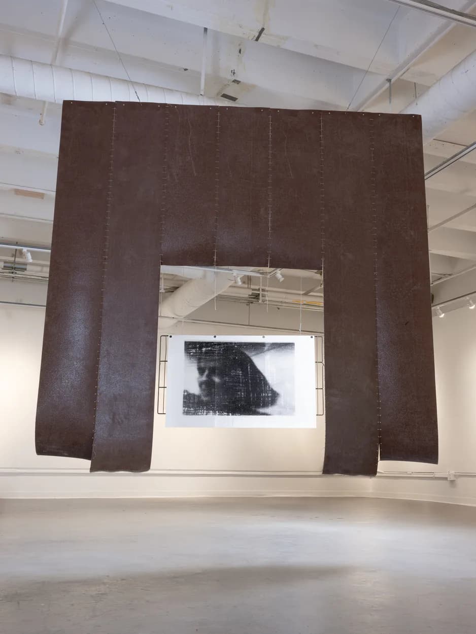 Large dark red burlap arch installation with suspended photographic print of obscured face in gallery
