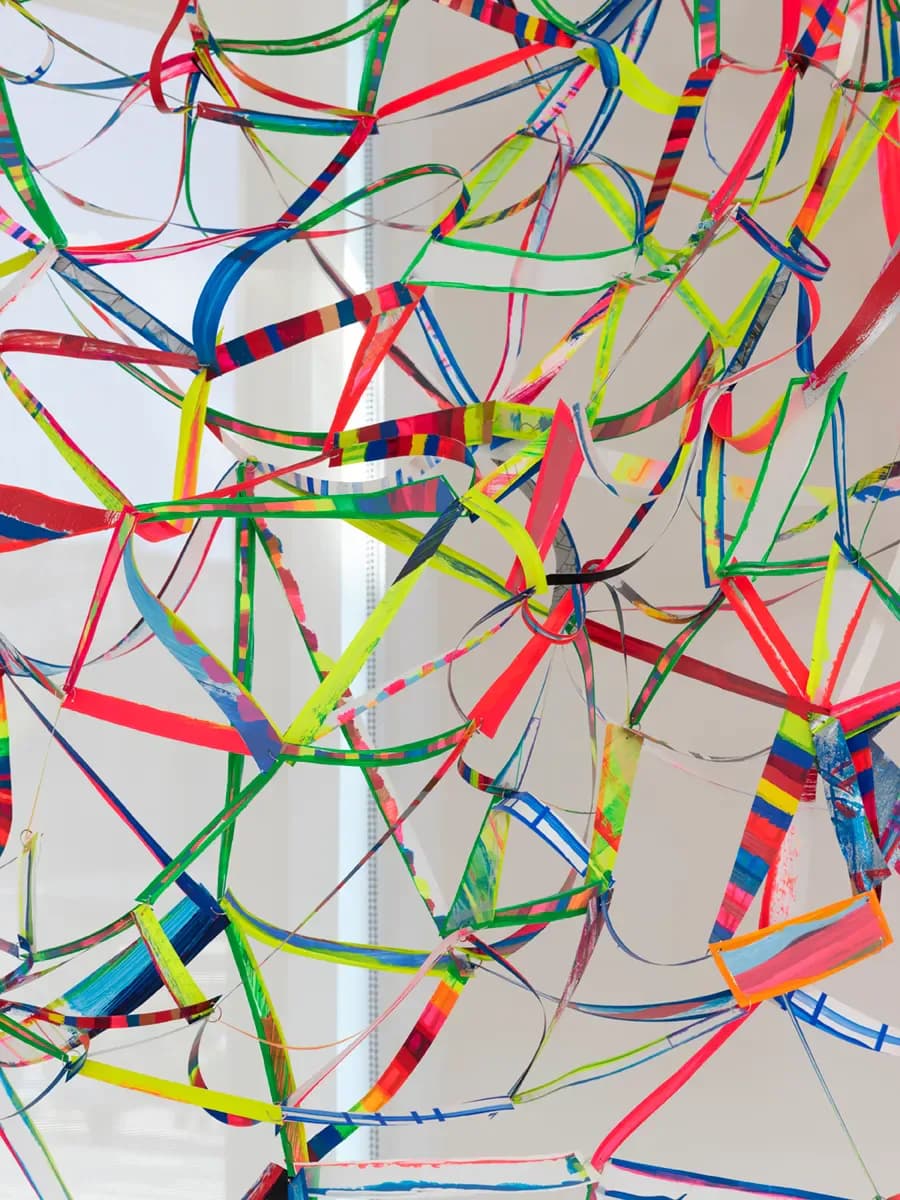 Tangled composition of multicolored ribbons and strips in red, blue, green, and yellow creating an explosive, chaotic abstract pattern against white.