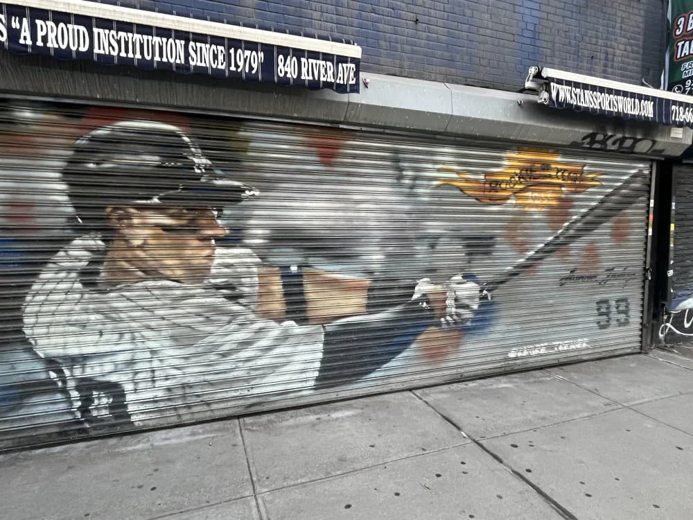 Mural of a baseball player in Yankees pinstripe uniform holding a bat, painted on a metal shutter with realistic detail.