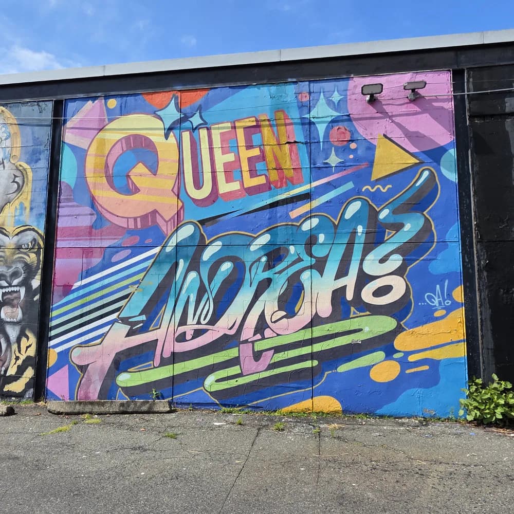 Colorful mural with 'QUEEN' in orange and 'ANDRES' in blue script against pink, blue, and yellow background with geometric and star elements.