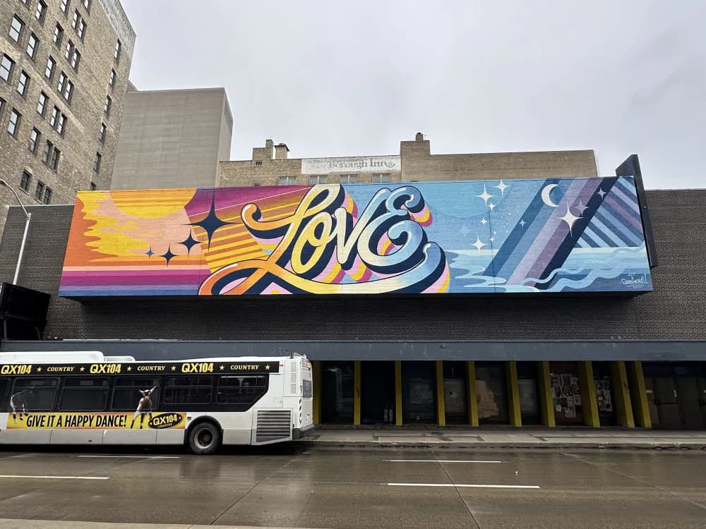 Wide mural featuring 'LOVE' in stylized yellow and purple script with flame motif on left, blue crystalline forms on right, mounted on dark storefront.