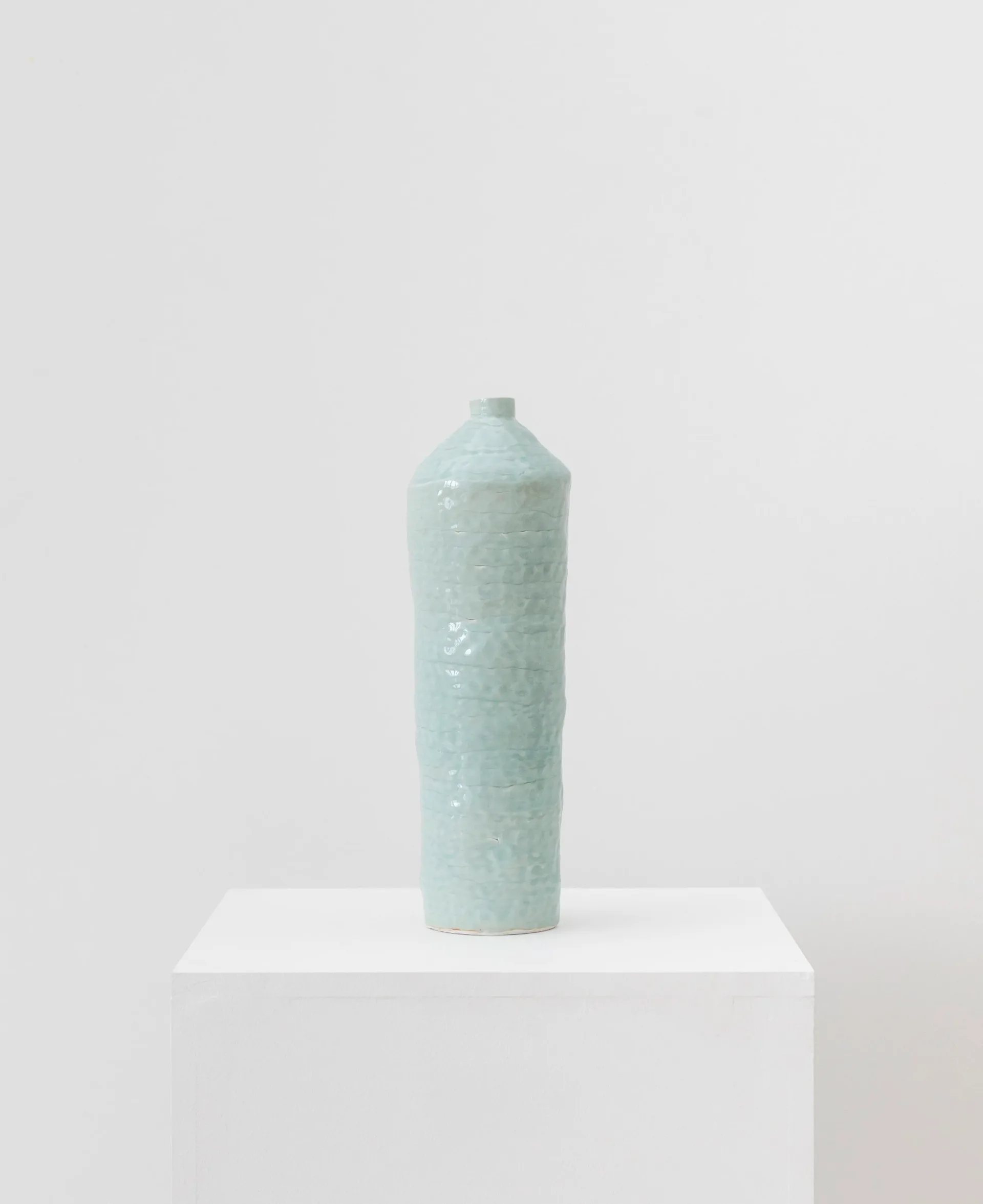 Tall celadon-glazed ceramic bottle form on white pedestal