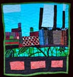 Textile quilt artwork depicting an urban cityscape with buildings and smokestacks
