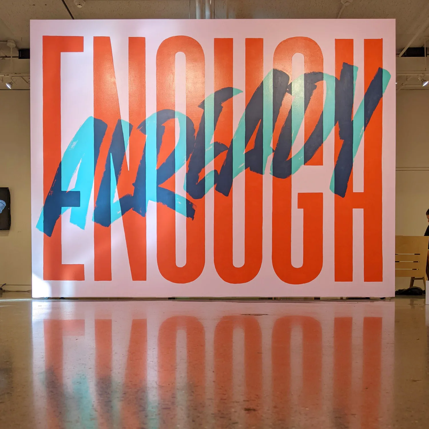Large-scale mural with bold orange typography reading 'ENOUGH', overlaid with geometric blue angular shapes and lines.