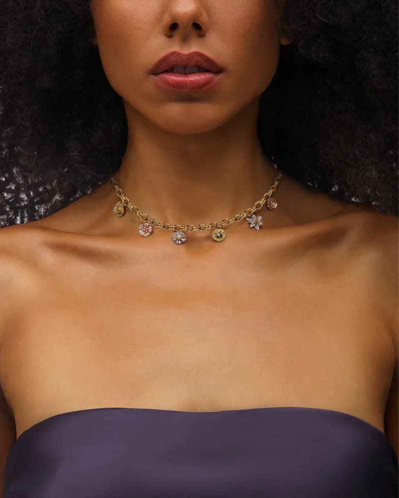 Gold chain necklace with hanging cluster of round diamond and gemstone pendants worn on model against dark background.
