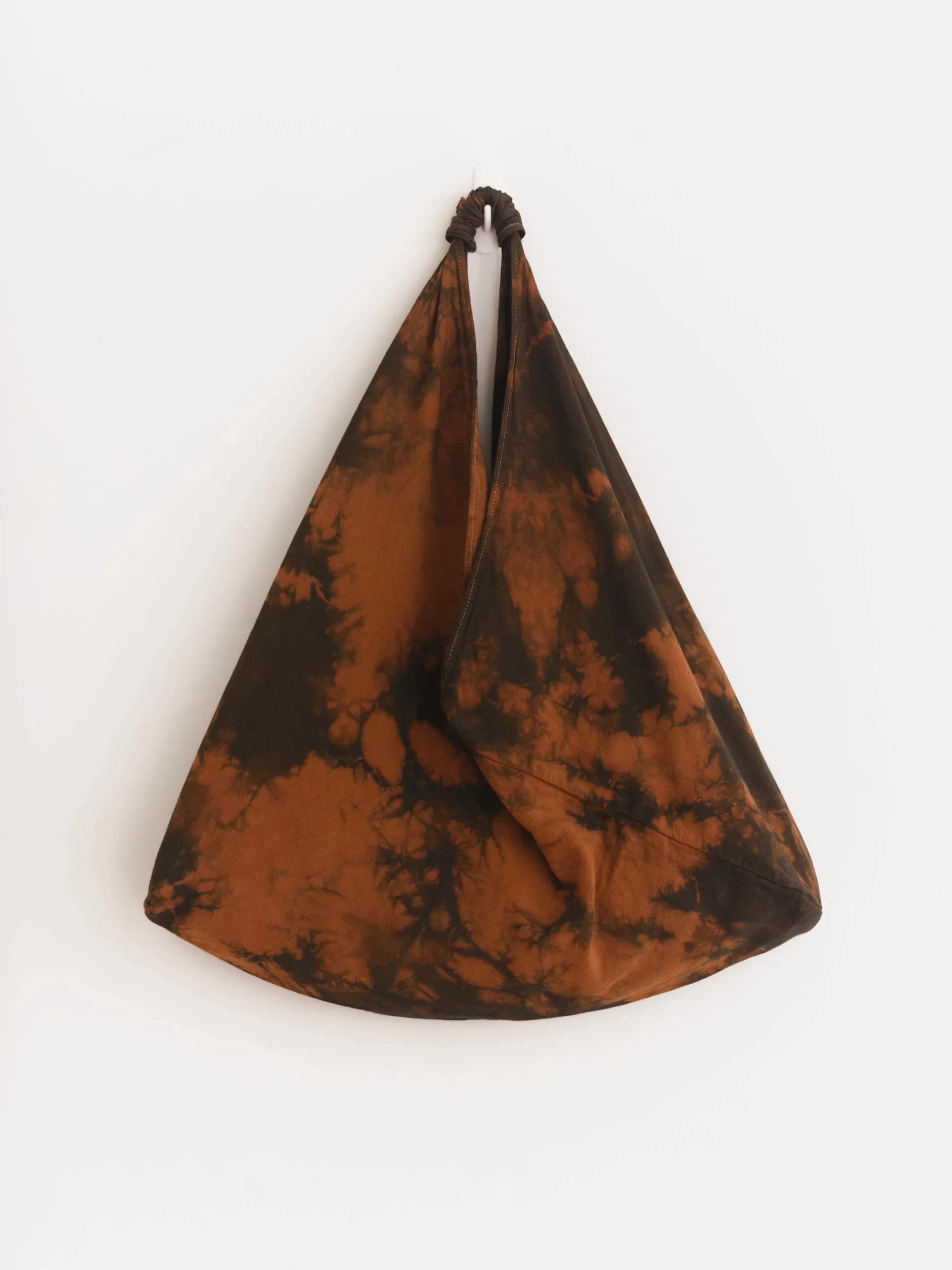 Brown and black shibori tie-dye triangular fabric bag hung against white wall