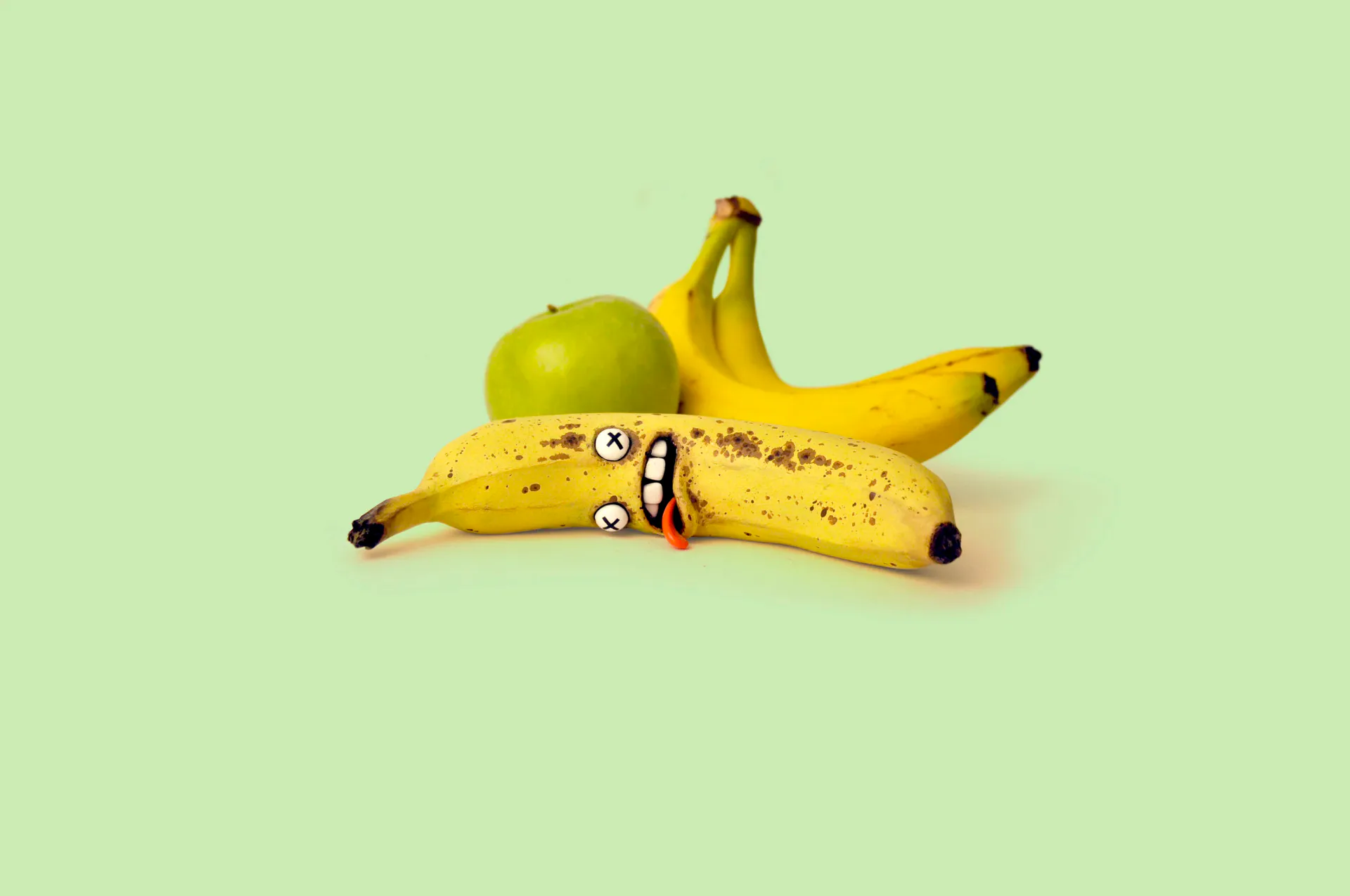 Animated banana with clay face lying among fruit on mint green background