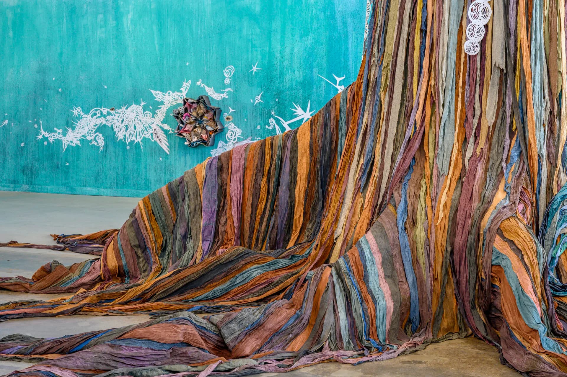 Large-scale cut-out figure of a woman with flowing colorful robes and intricate botanical imagery, standing in an industrial gallery space