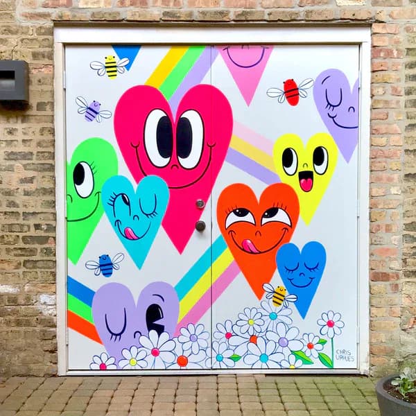 Completed mural of smiling heart characters with rainbows and daisies painted on a garage door set in a brick wall