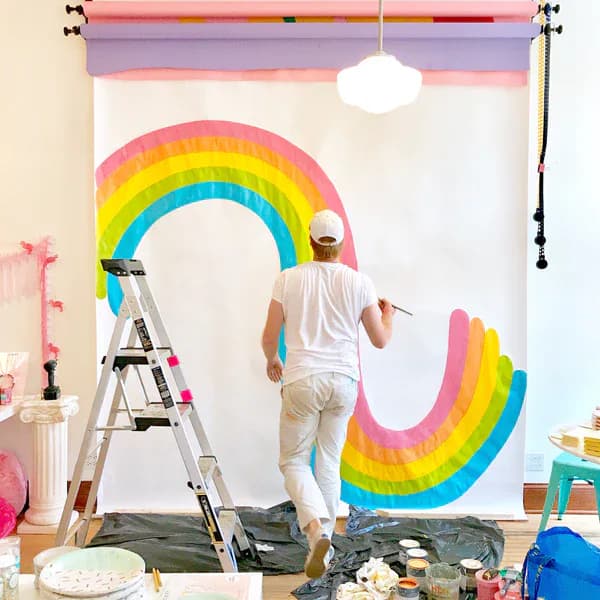 Colorful storefront window paintings featuring cartoon sun, hearts, rainbow and ladybug characters on a pink building