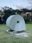 Large circular stone sculpture with hole, installed outdoors on grass at dusk