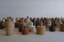 Installation of hundreds of small ceramic cylinder sculptures arranged on a floor