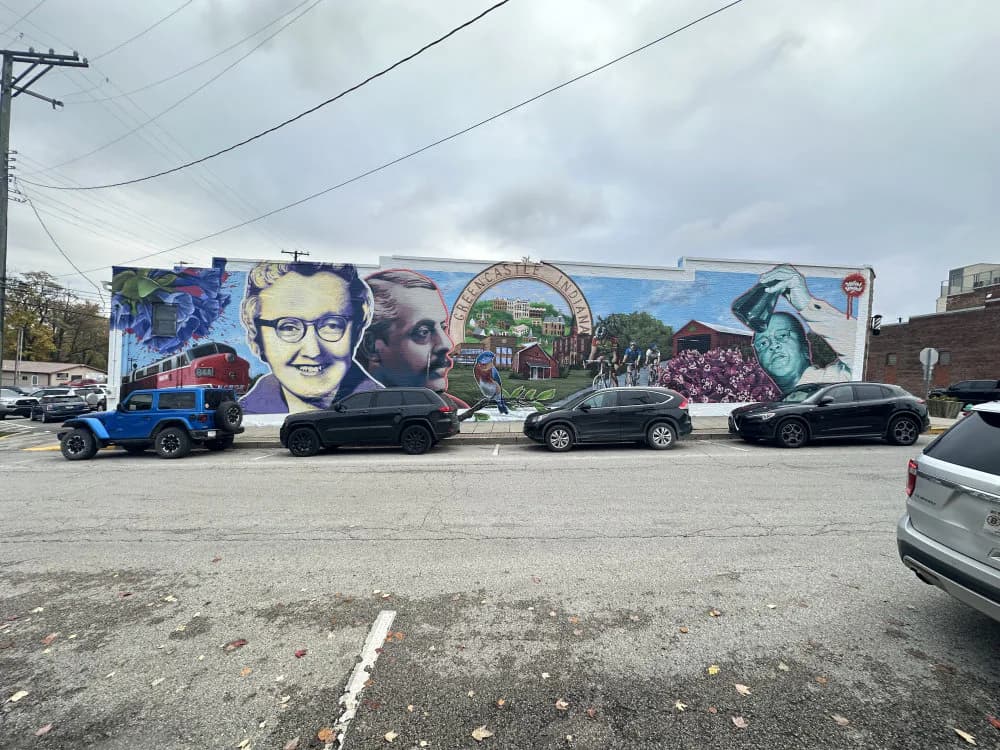 Large-scale mural with multiple portrait panels in blue, white, and natural tones, including profiles and a circular emblem, spanning across a building facade.