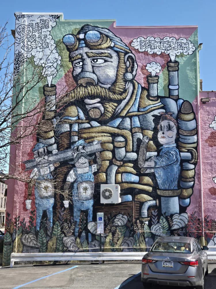 Large-scale mural by Denton Burrows depicting a bearded man with goggles and mechanical body parts, rendered in blue, green, and pink tones on a building facade.