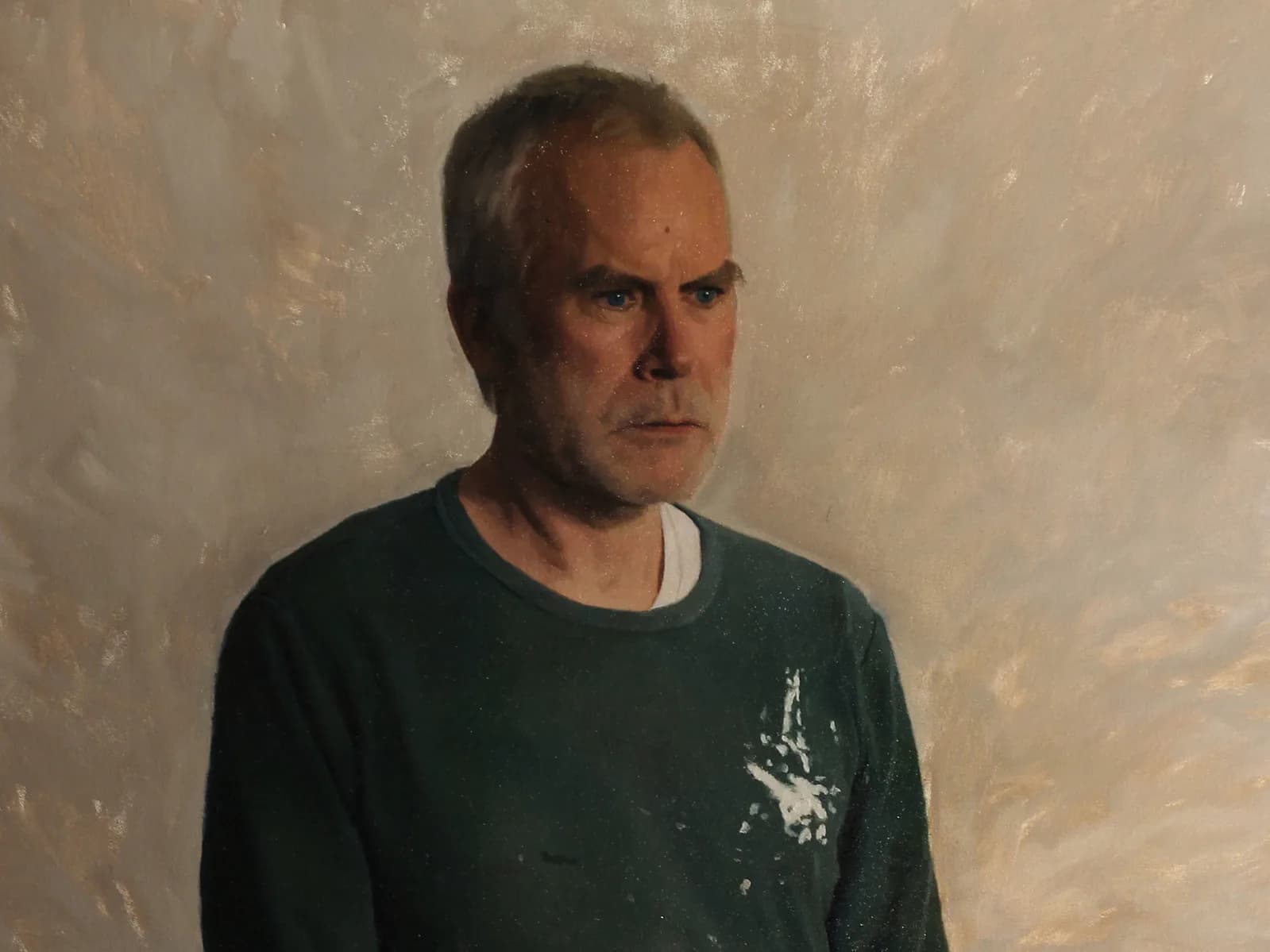 Middle-aged man with receding hair wearing dark green t-shirt with graphic print, neutral expression against textured wall.