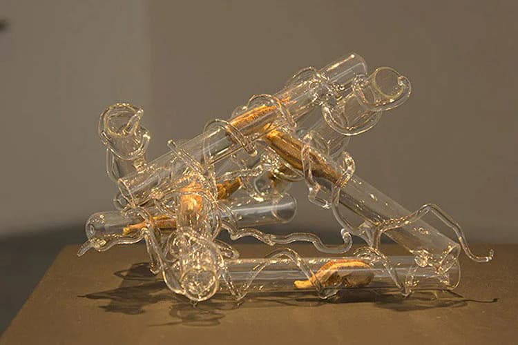 Transparent glass sculpture with golden internal elements, depicting an abstract mechanical or organic form, photographed against neutral background with dramatic lighting.