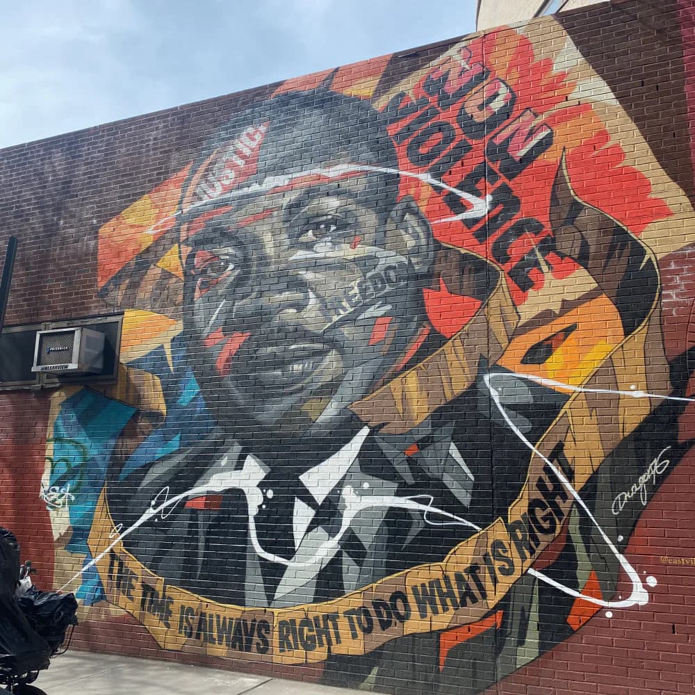 Mural portrait of a man in formal attire with geometric patterns in red, orange, and gold on brick wall; text reads 'I HAVE A RIGHT TO DO WHAT I WANT.'
