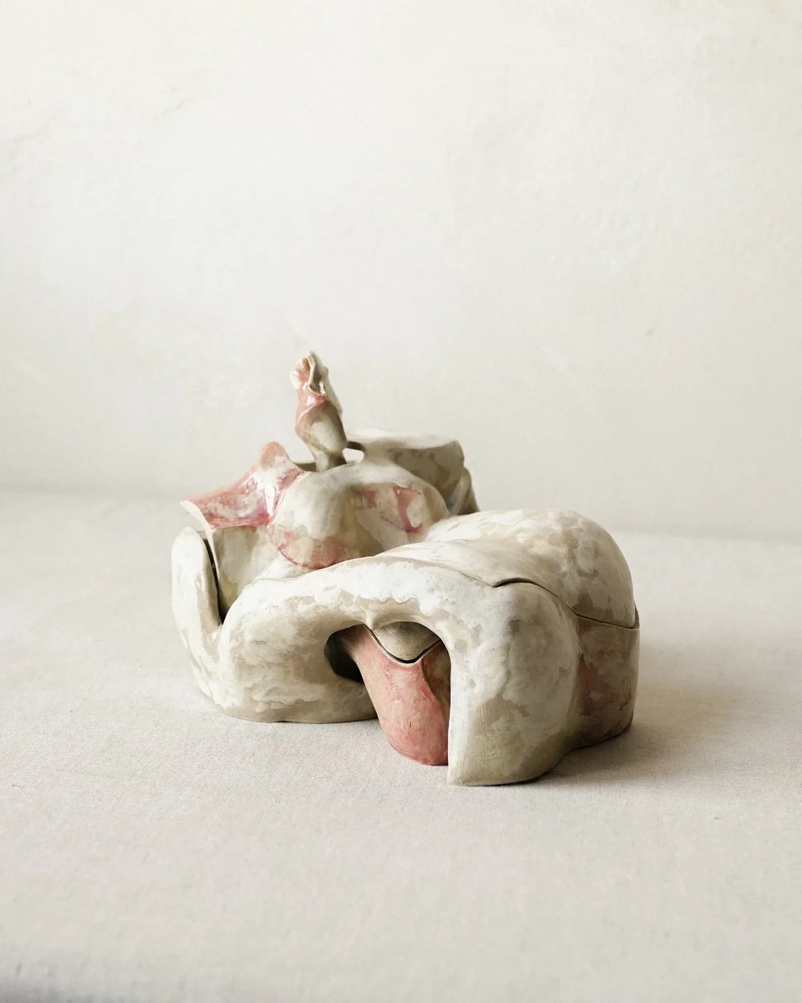 Organic ceramic sculpture with pink and white mottled glaze featuring figurative elements