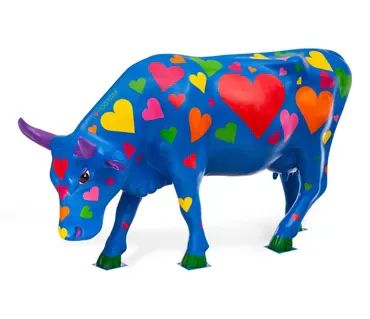 Painted sculpture of a blue cow with multicolored heart and geometric shapes covering its body, standing on white background.