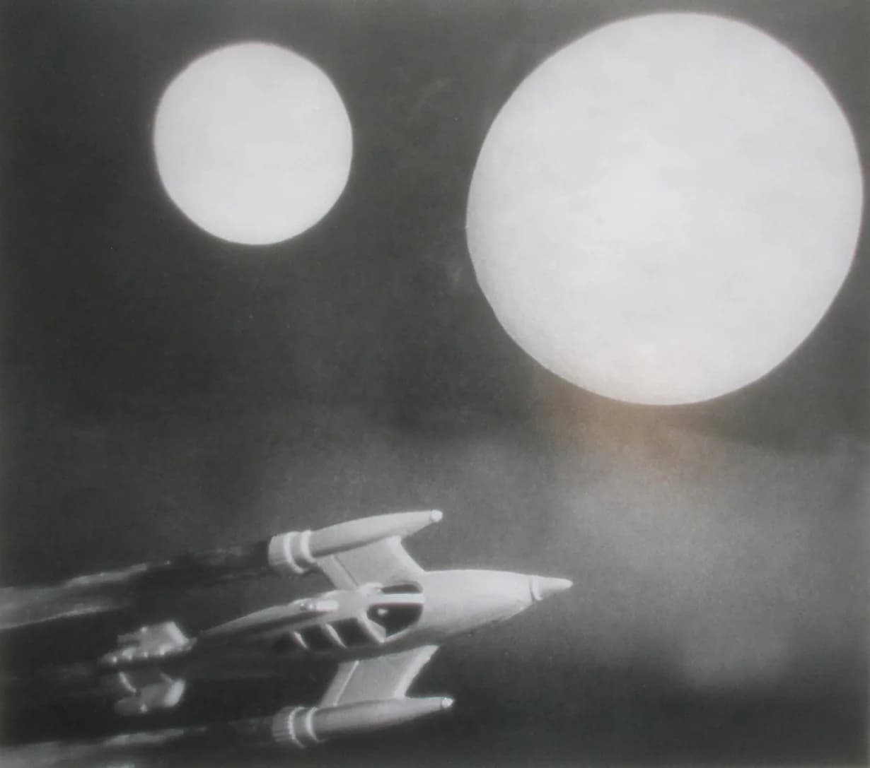 Spaceship model against dark sky with two large glowing orbs, black and white photomontage