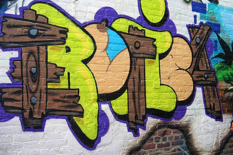 EROTICA 67 street art mural featuring large-scale graffiti letters in lime green and brown wood textures with purple outlines on white brick wall.