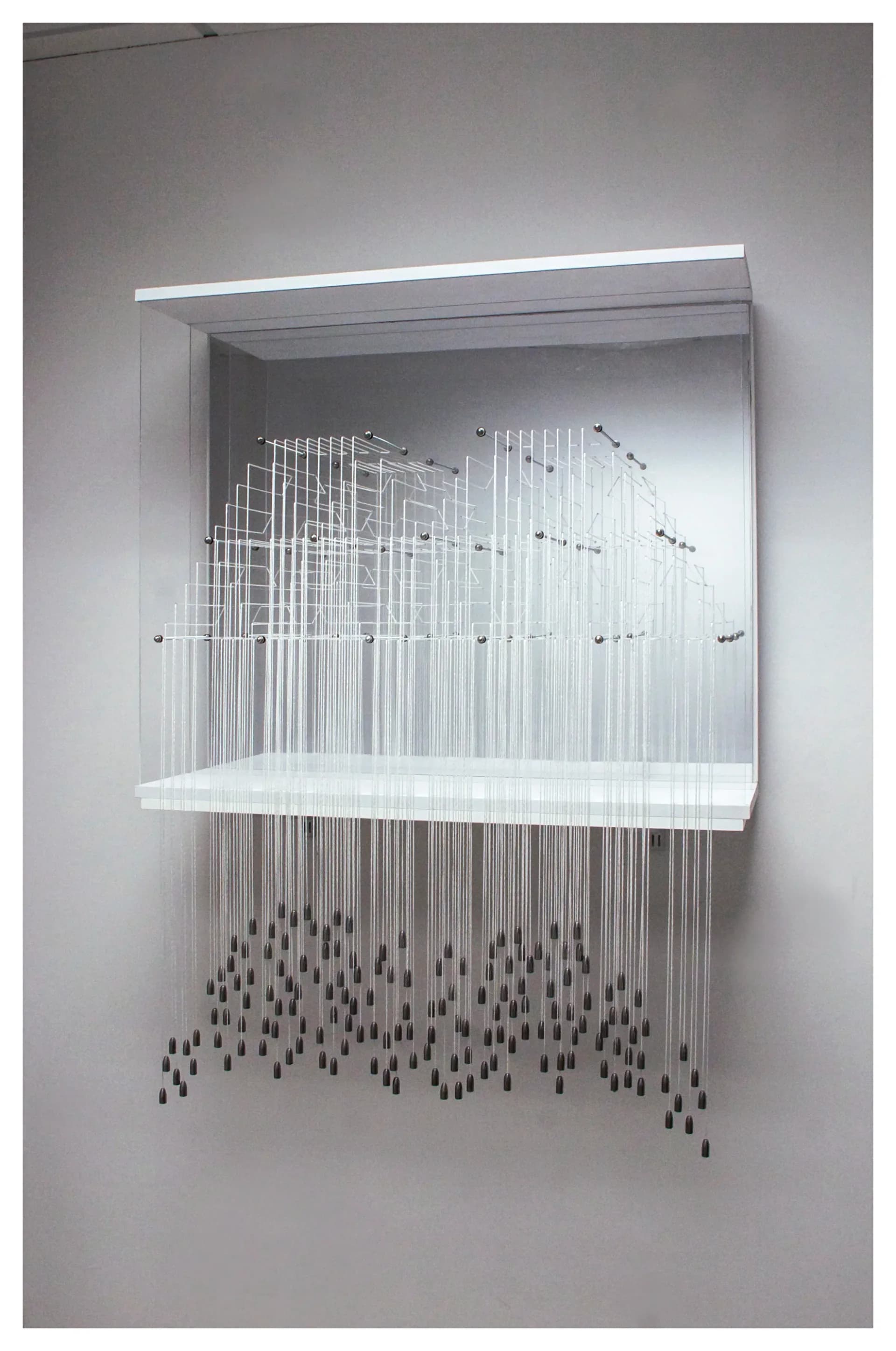 Large wall-mounted installation with acrylic panels, white thread warp, and hanging weighted pendants in a white gallery space