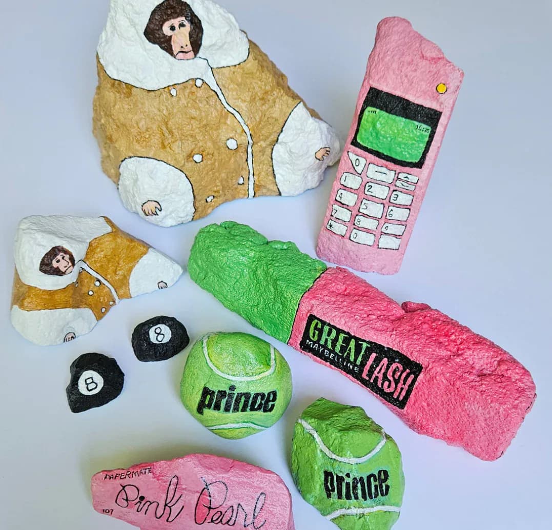 Handmade textile and plush sculptures including stuffed animals with faces, a pink phone, a neon-green tennis bag, and Prince-branded green tennis balls arranged on white background.