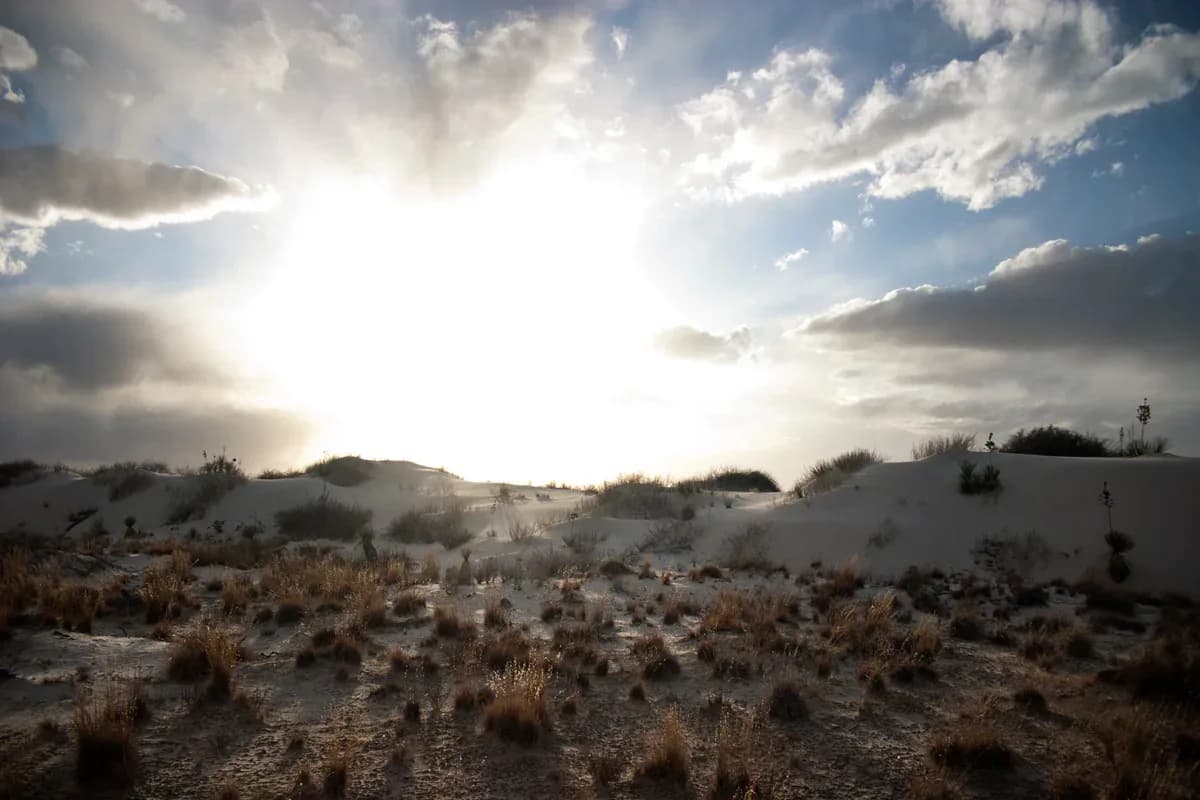 White sand dunes landscape with dramatic backlit sun breaking through clouds