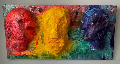 Three colorful sculptural faces in red, yellow, and blue-purple on a painted mixed-media background