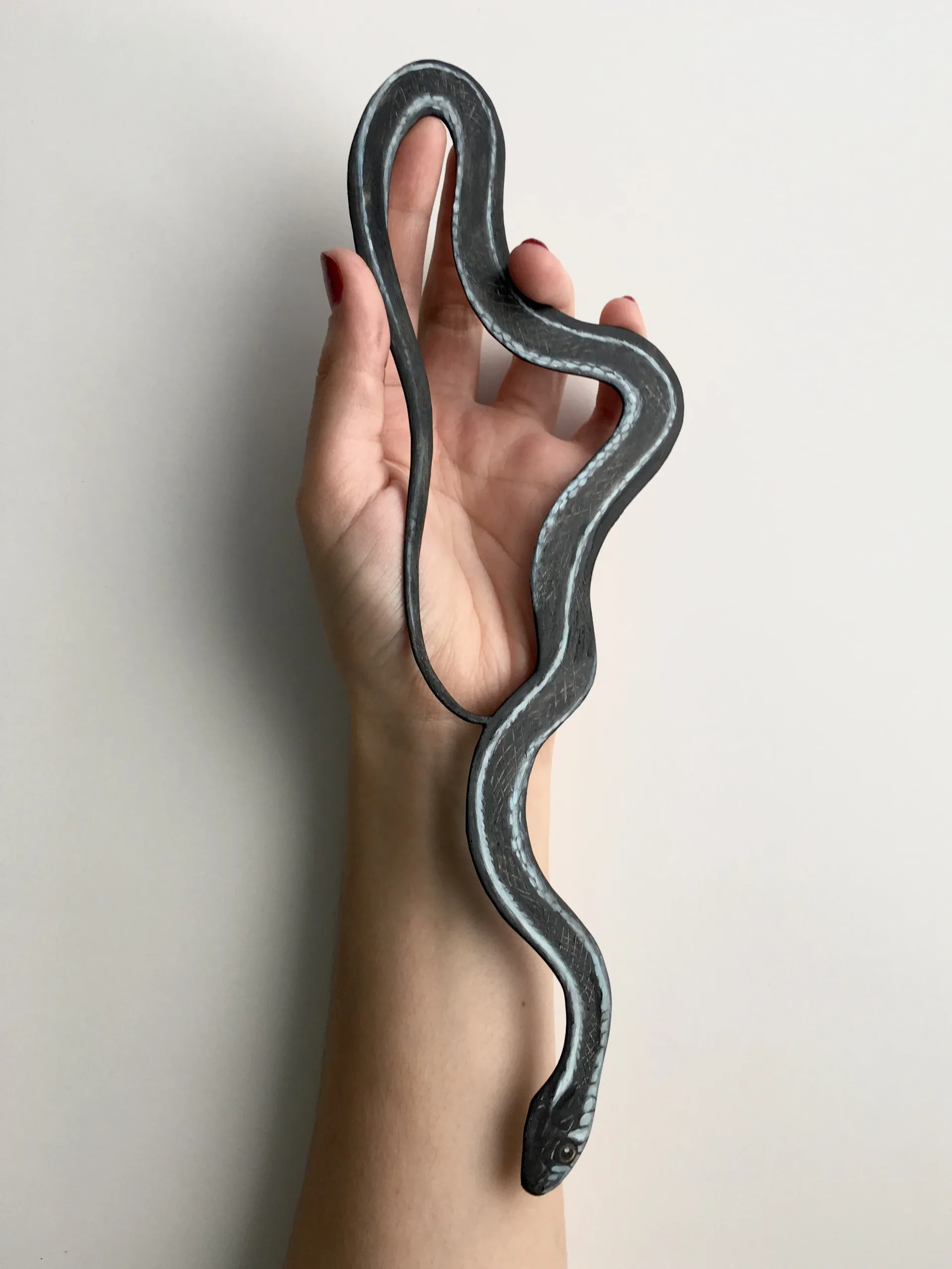 Hand holding a three-dimensional gray and pink sculptural snake form curving upward.