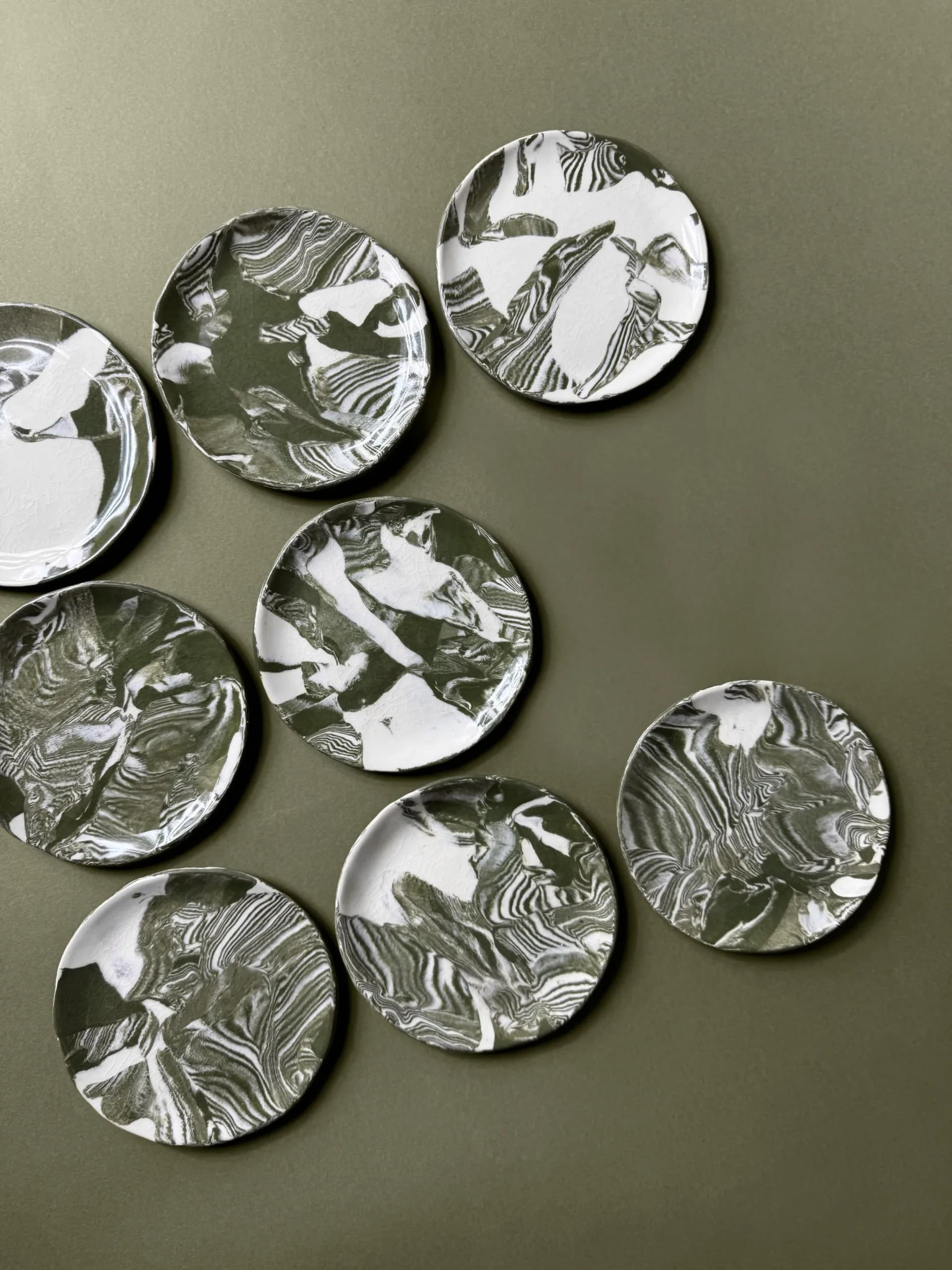 Set of seven black and white marbled ceramic plates arranged on olive green surface