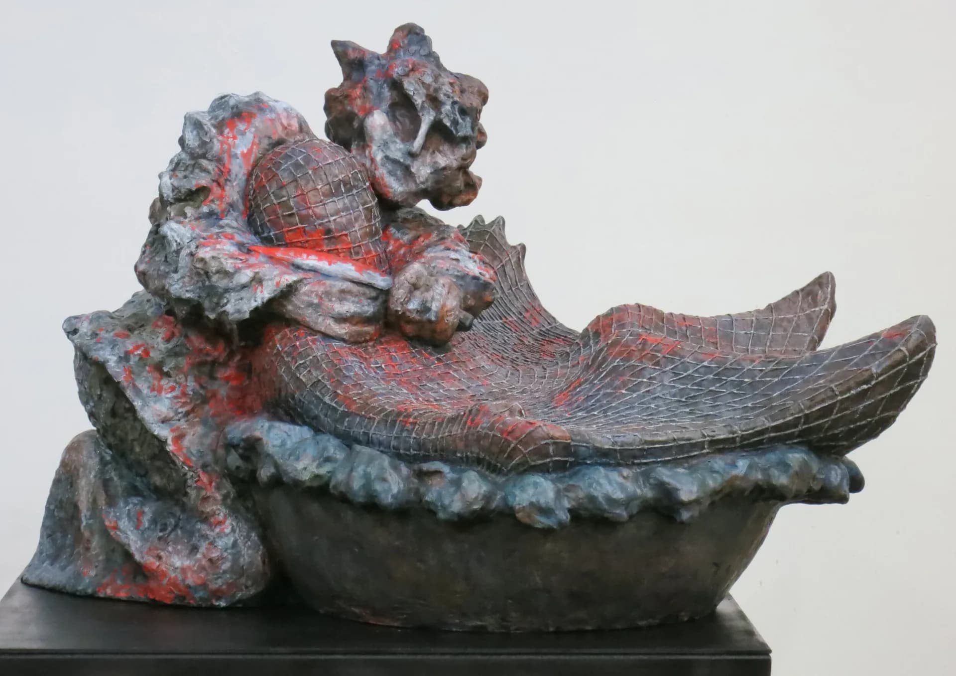 Painted sculpture of a dragon-like figure reclining in a boat with red and grey tones