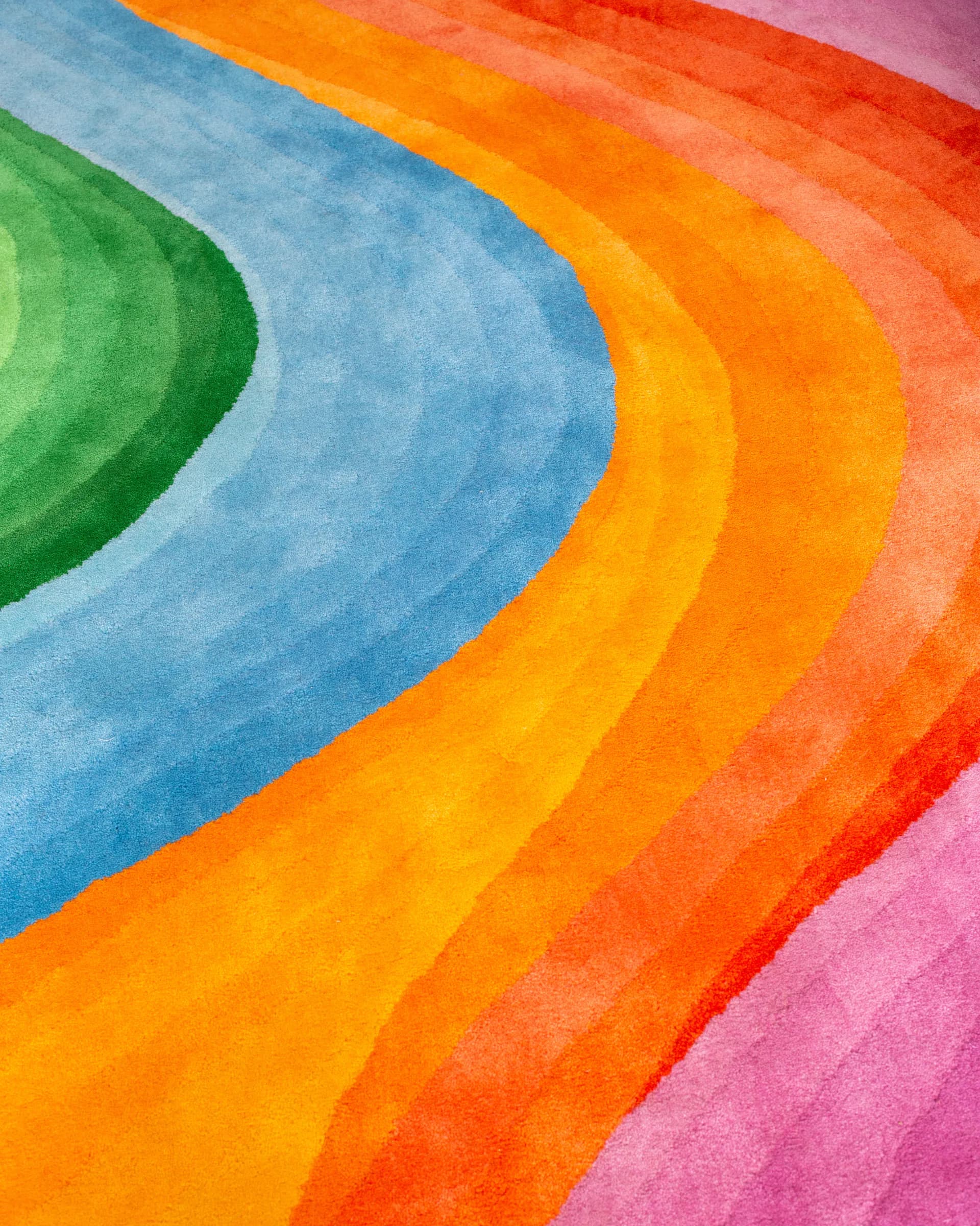 Close-up detail of a tufted rainbow wave rug showing rich color gradients in blue, green, orange, and pink