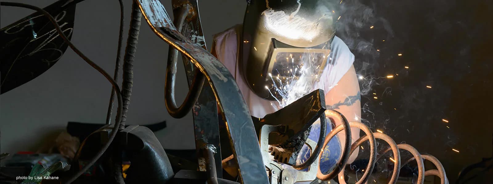 Welded metal sculpture with orange-glowing elements creating abstract form with sparks visible.