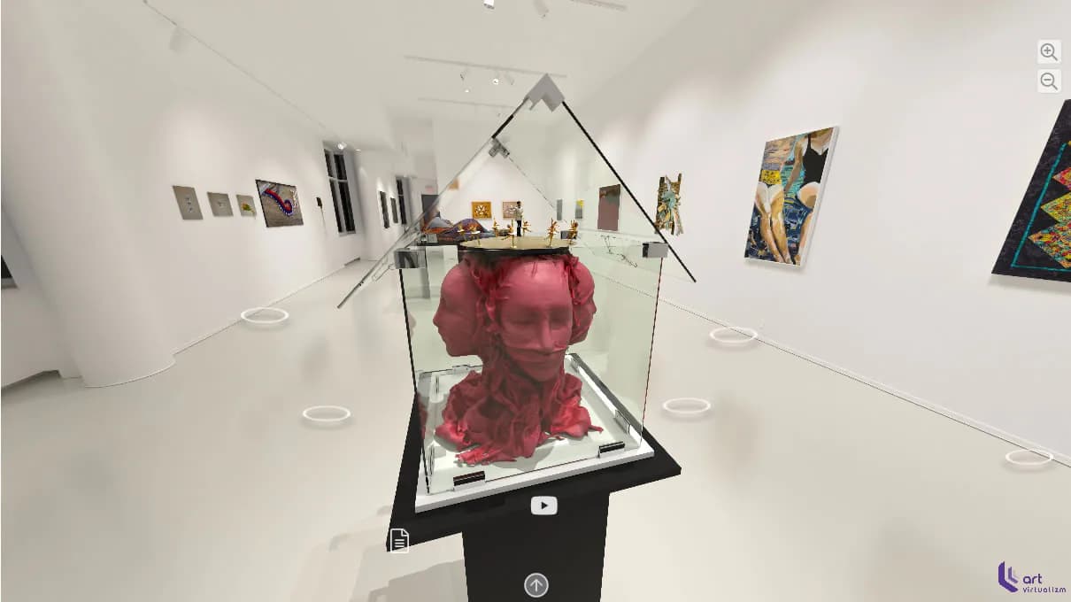 Gallery interior with white walls displaying a red sculptural head in a glass case, surrounded by framed artwork and gallery lighting.