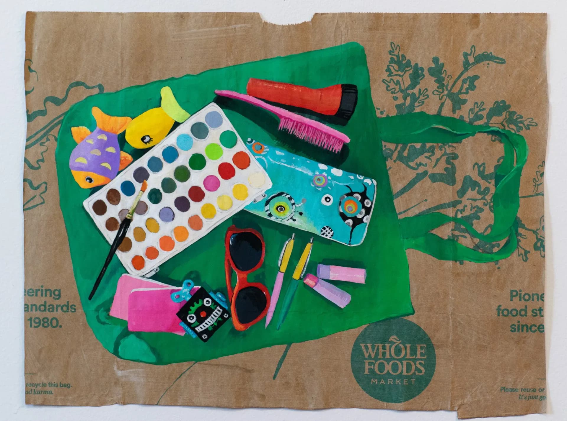 Painting of colorful everyday items including watercolor palette, sunglasses, and toys spread on a green tote bag over a Whole Foods paper bag