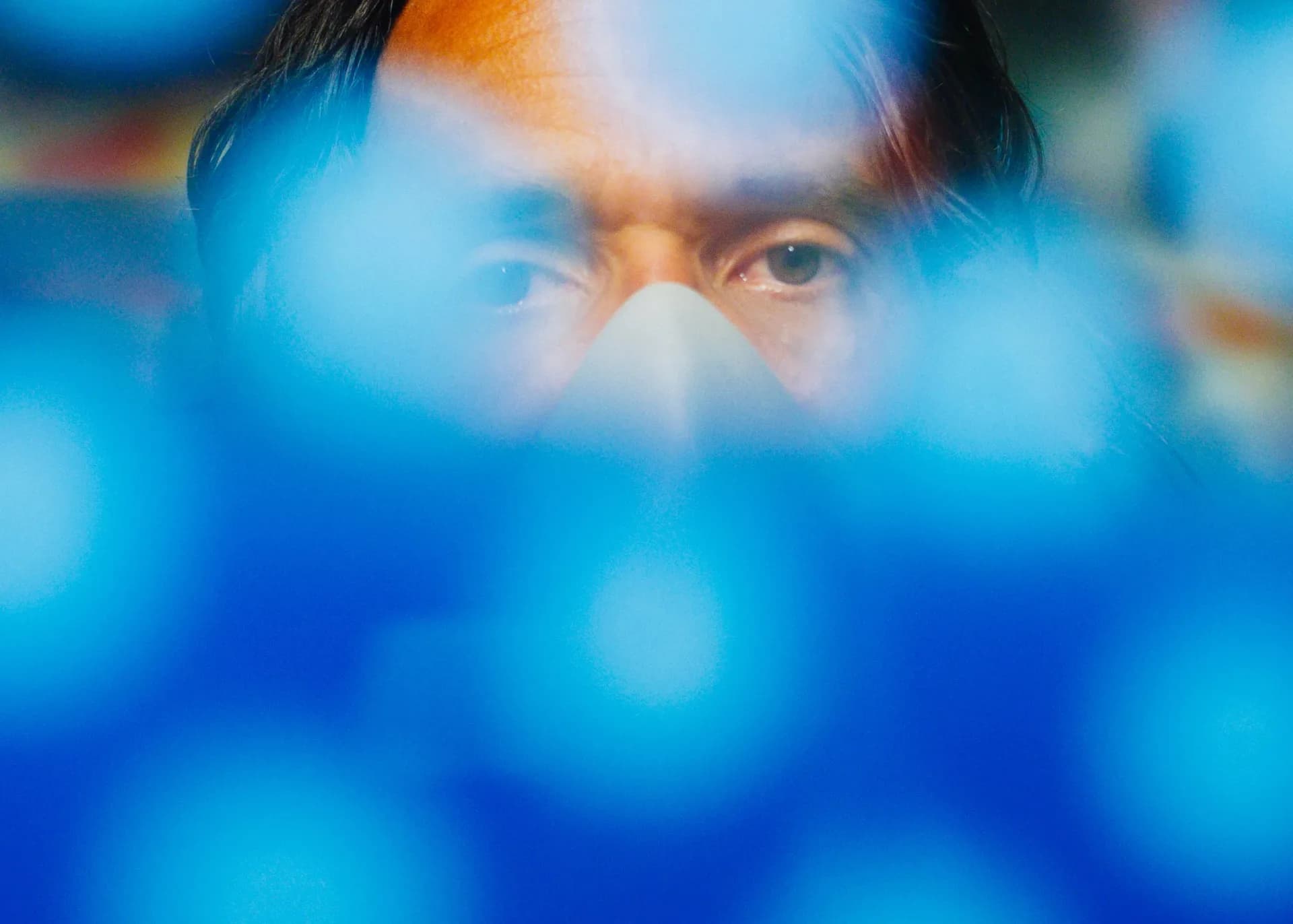Close-up portrait with blue bokeh effect and warm light highlighting a person's eyes and nose through soft focus.