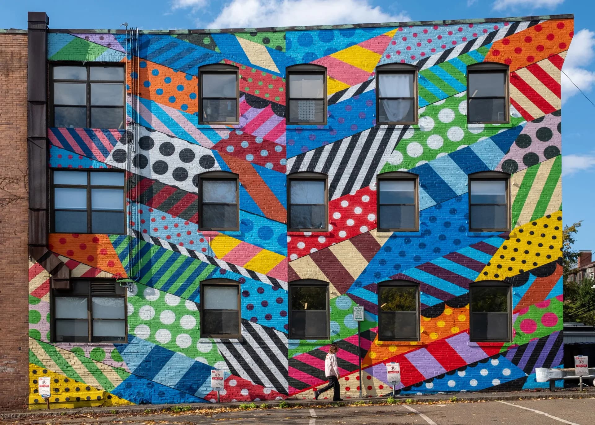 Large-scale mural on building facade featuring vibrant geometric patterns, polka dots, stripes, and bold colors covering multiple windows.