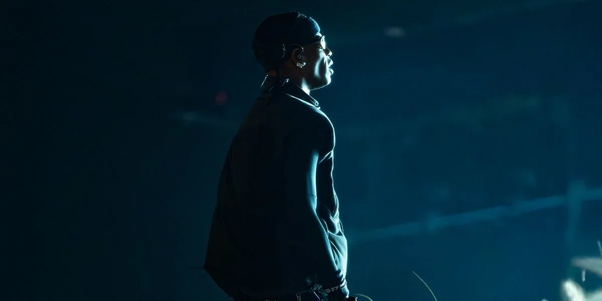 Silhouetted figure in dark clothing against teal and blue gradient background with atmospheric lighting.
