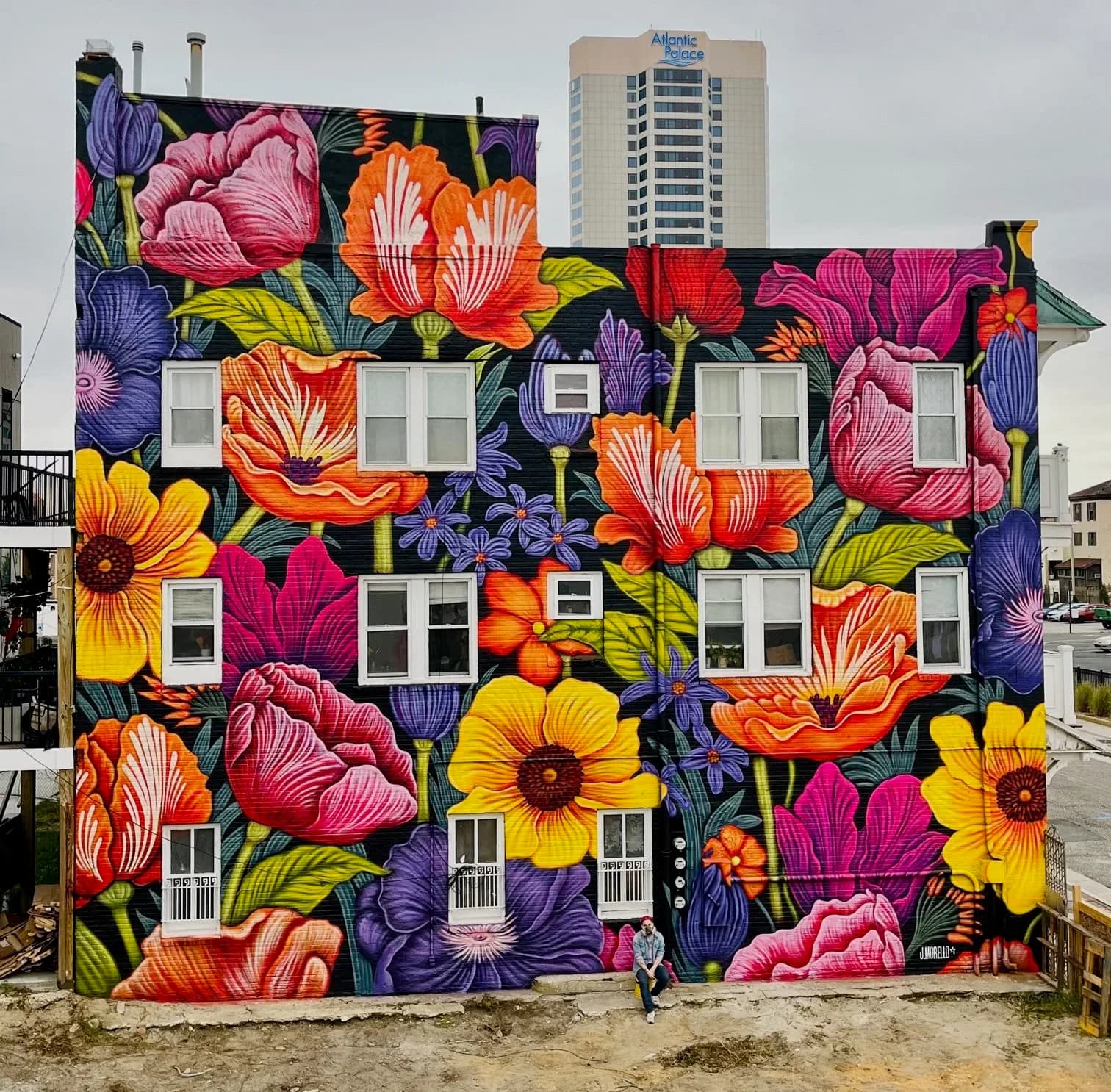 Large-scale floral mural covering entire building facade with vibrant poppies, tulips, and sunflowers on black background, Atlantic City NJ