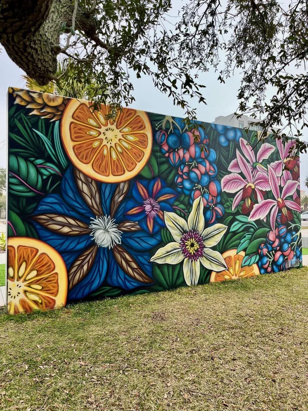 Large outdoor mural of lion peeking through colorful tropical flowers and blue leaves