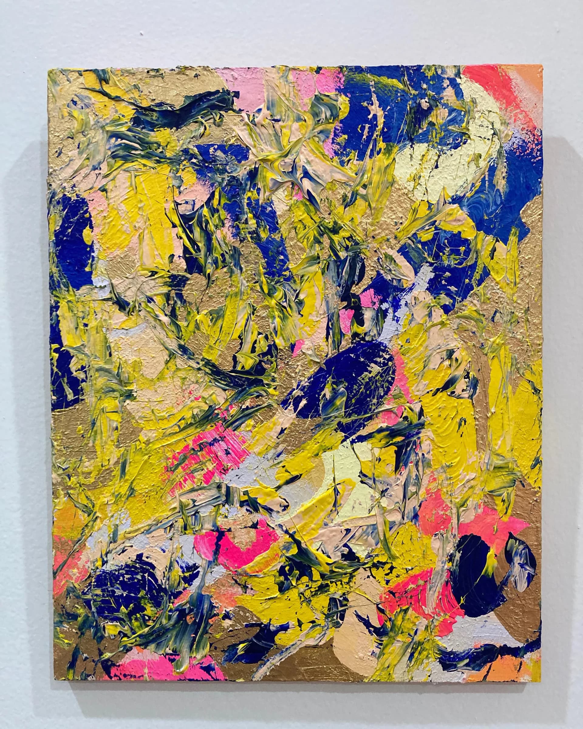 Energetic impasto abstract painting in yellow, blue, pink, and gold tones hung on white wall