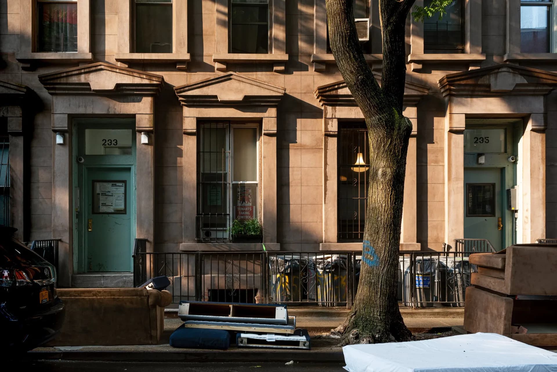 Sunlit brownstone facades with discarded furniture on the sidewalk