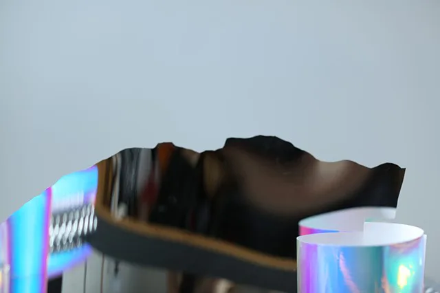 Close-up of a sculptural installation featuring iridescent holographic cylindrical forms alongside a dark reflective irregular surface