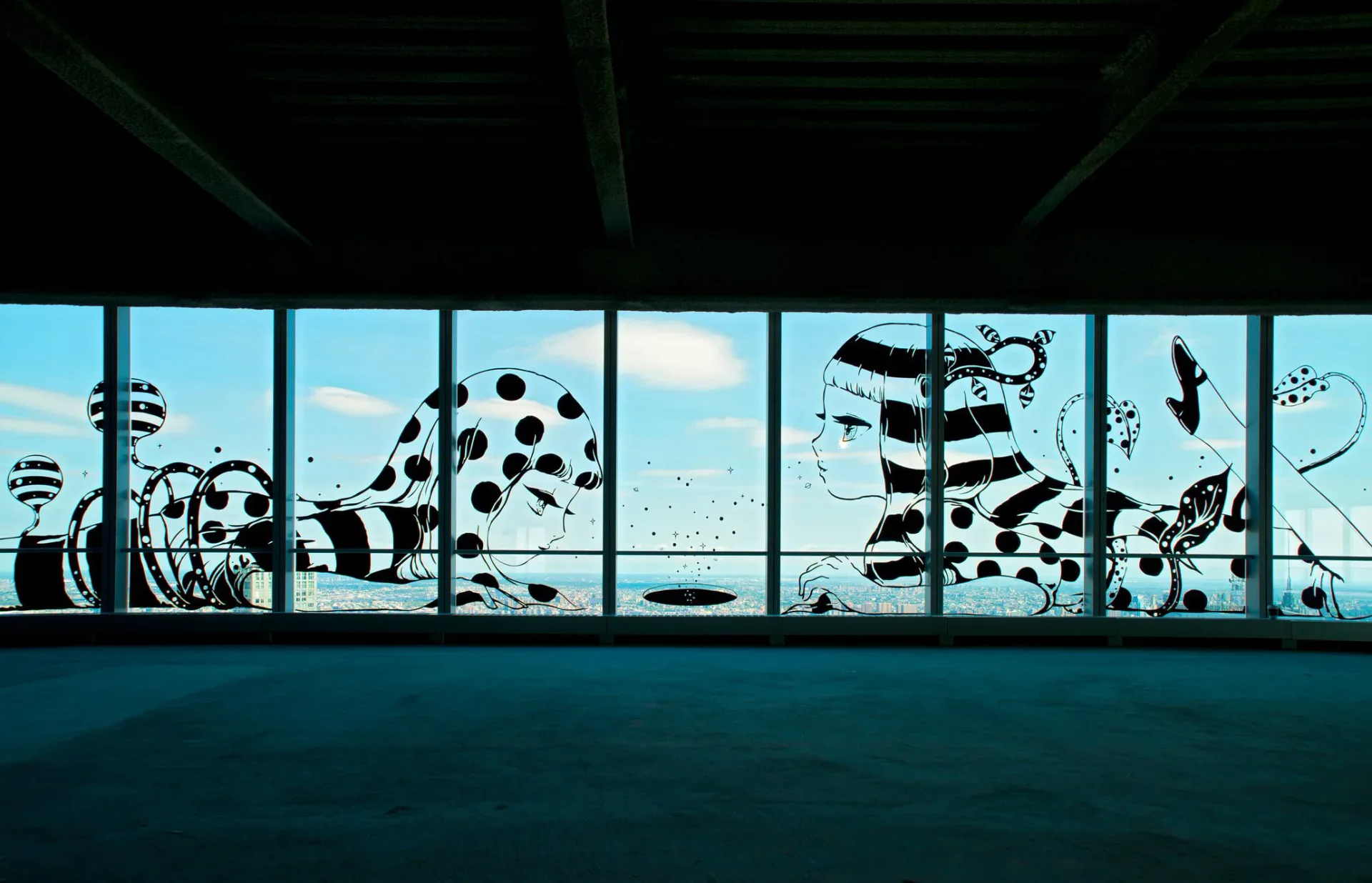 Black and white window mural of reclining anime-style figures with polka dots and stripes against a city skyline panorama