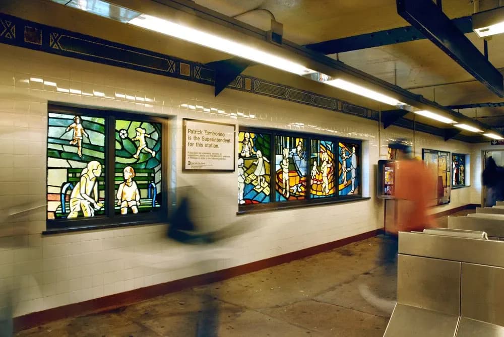 Interior photograph of a transit station with stained-glass style illuminated panels displaying figures against a cream-colored wall.