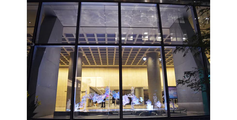 Large-scale iridescent acrylic and LED installation in a building lobby seen from outside at night